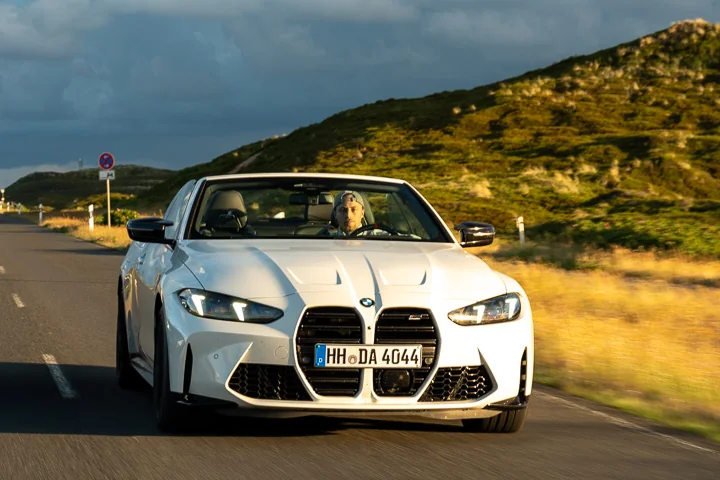 BMW M4 Competition Cabrio fährt im Abendlicht über eine Dünenstraße auf Sylt