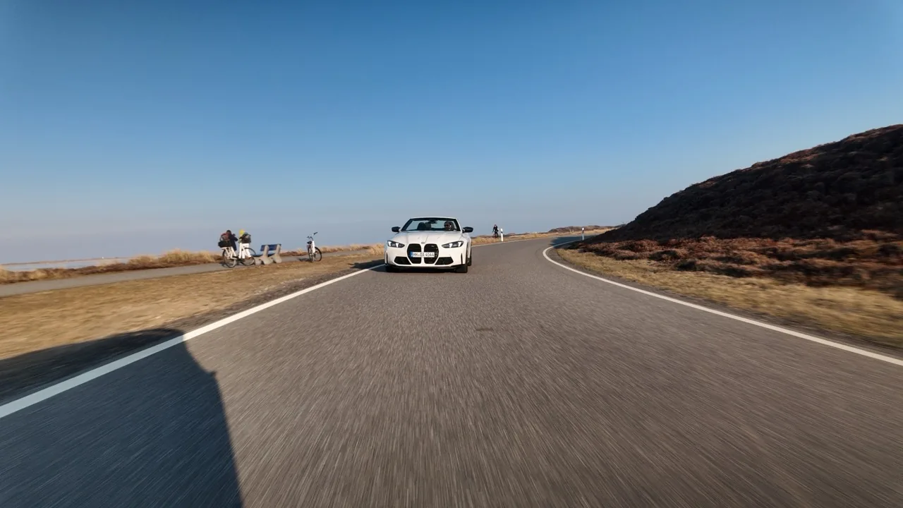 BMW M4 Competition Cabrio in Alpinweiß auf einer Sylter Inselstraße zwischen Heide und Dünen — Drohnenaufnahme bei Tageslicht